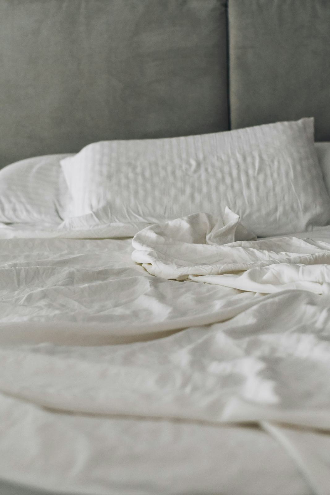 A neatly made bed with white linens in morning light