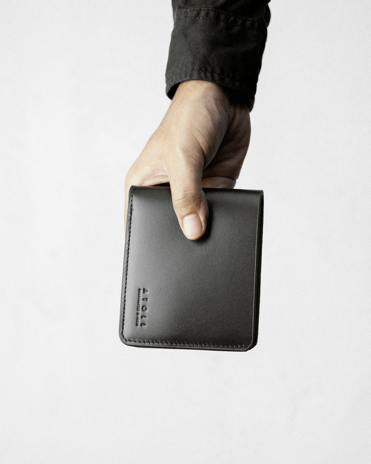 A hand holding a black leather wallet in moody light