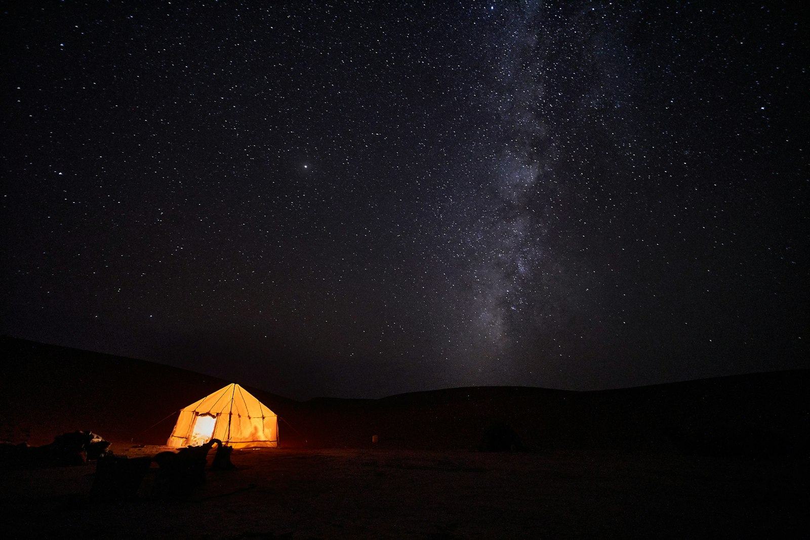 A lit tent in a field under a starry night sky